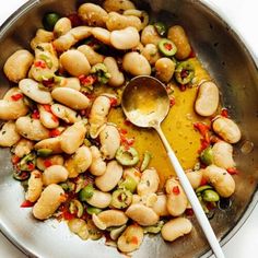 a silver bowl filled with beans and vegetables next to a spoon on top of a table