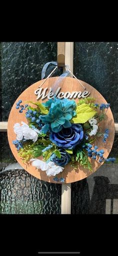 a welcome sign hanging on the side of a building with flowers in it and leaves