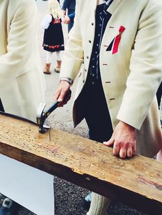 a man wearing a suit and tie cutting a piece of wood