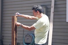 a man is using a pair of scissors to trim a piece of wood on the side of a house