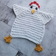 a crocheted chicken is laying on the floor in front of a marble wall