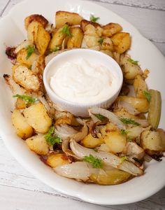 a white plate topped with potatoes and onions next to a small bowl of ranch dressing