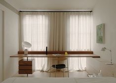 a bedroom with a bed, desk and window in the corner that has sheer curtains