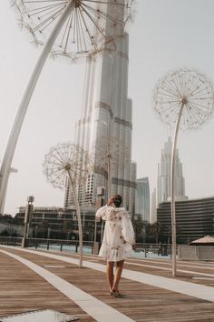 a woman in a white dress is walking on a boardwalk with ferris wheel and buildings in the background