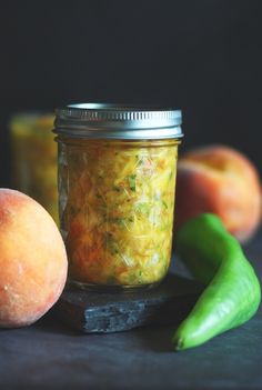 two peaches and some pickles on a table next to a jar of food