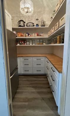 an open pantry with white cabinets and wooden counter tops in the middle of it is lit by a chandelier hanging from the ceiling