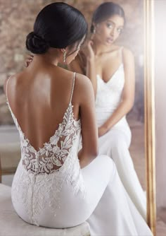 a woman sitting in front of a mirror looking at her reflection wearing a wedding dress