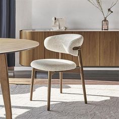 a white chair sitting next to a wooden table in front of a cabinet and vase