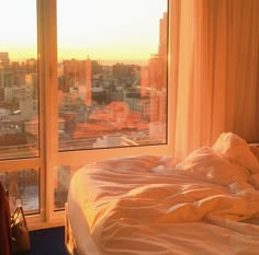 an unmade bed sitting in front of a window with cityscape behind it