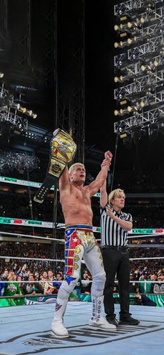 two men standing on top of a wrestling ring holding their hands up in the air