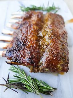 a piece of meat on a white plate with rosemary sprigs