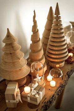 three wooden christmas trees sitting on top of a table next to candles and boxes filled with presents