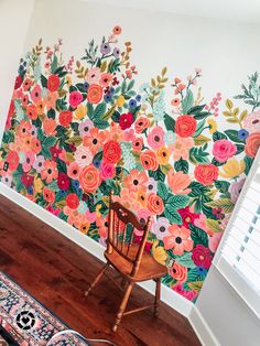 a chair sitting in front of a wall with flowers painted on it and a rug next to it