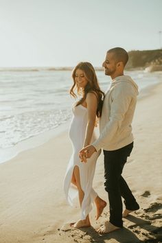 a man and woman walking on the beach holding hands