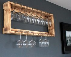 wine glasses are lined up on a wooden shelf in front of a gray wall and framed photograph