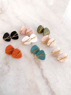 six pairs of ear clips in different colors and sizes on a marble surface with gold wire