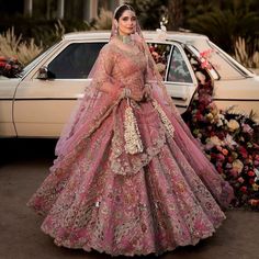 a woman standing in front of a car wearing a pink bridal gown