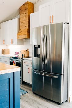 a stainless steel refrigerator in a kitchen with white cabinets and blue island countertop area