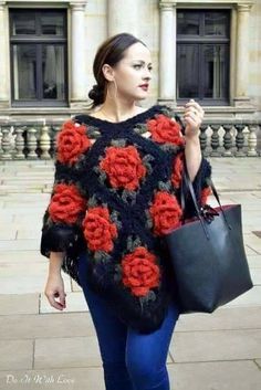 a woman walking down the street carrying a black bag and wearing a red rose sweater