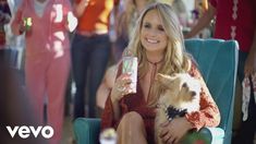 a woman sitting in a chair holding a small dog and drinking from a canister