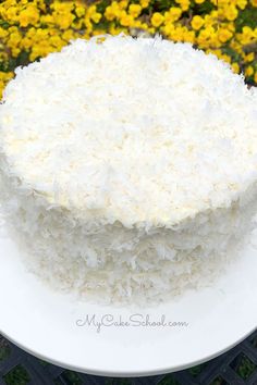 a white cake sitting on top of a white plate next to yellow and purple flowers