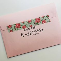 an open pink envelope with floral ribbon on the top and words written in black ink