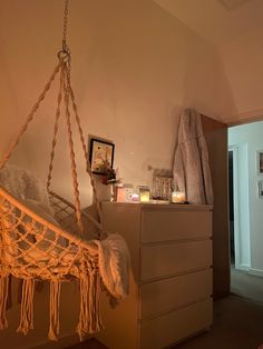 a hammock hanging from the ceiling next to a dresser with candles on it