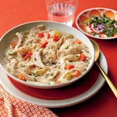 a bowl of chicken and dumpling soup on a red tablecloth next to a glass of water