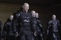 a group of men standing next to each other wearing black leather suits and holding swords