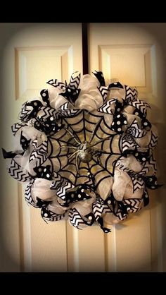 a spider web wreath hanging on the front door with black and white ribbons around it