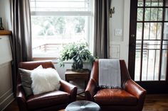 two brown leather chairs sitting in front of a window