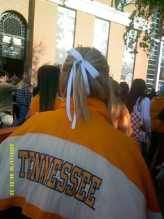 a woman in an orange and white jacket with a bow on her head standing next to a group of people