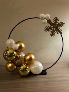 a christmas decoration with gold and white balls in a circle on top of a wooden table