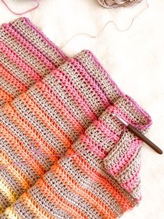 a crocheted blanket with yarn next to it and knitting needles on the ground