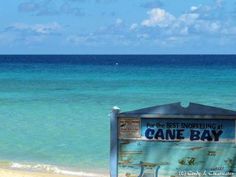 a sign that is sitting on the sand near the water's edge with an ocean in the background