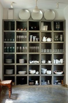 a room filled with lots of white dishes and cups on shelves next to a wooden chair