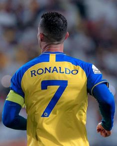 a soccer player in yellow and blue uniform with his hands behind his back as he looks at the ball