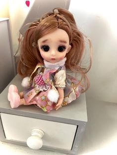 a doll sitting on top of a white dresser next to a drawer with drawers and knobs