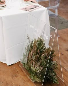 the table is set up for an event with white linens and greenery on it