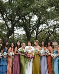 a group of women standing next to each other holding bouquets in front of trees