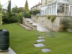 a garden with grass and stepping stones in the middle, next to a stone wall