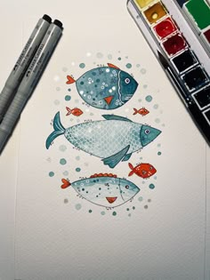 a drawing of two fish on top of a white paper with watercolor paints next to it