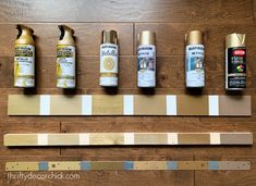 several different types of spray paint are lined up on a wooden board with gold trim