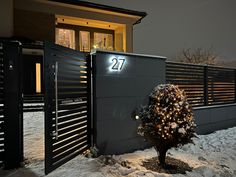 a small tree is lit up in front of a house with a number 27 on it