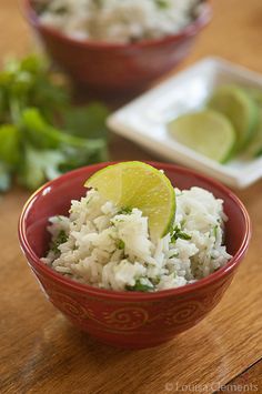 a red bowl filled with rice and lime wedges on top of a wooden table