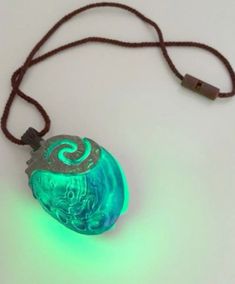 a necklace with a glowing green object on it's side and a cord attached to it