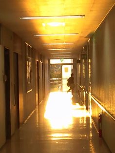 a person sitting on the ground in an empty hallway with sunlight coming through the windows