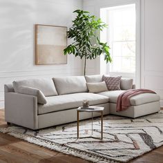 a living room with white walls and wood flooring, a large sectional couch in front of a potted plant