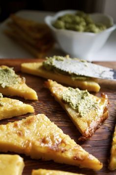 several slices of pizza on a wooden cutting board with pesto and cheese toppings