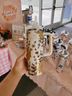 a person holding up a coffee mug in front of a table with cups on it